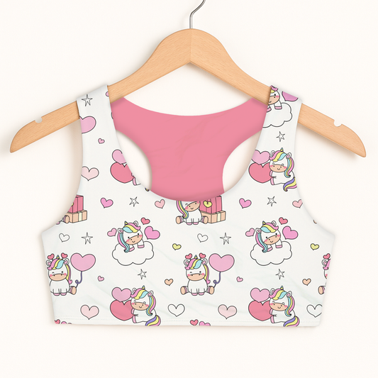 Pink girls sports bra with a white crop top featuring unicorn designs on a hanger against a white background.