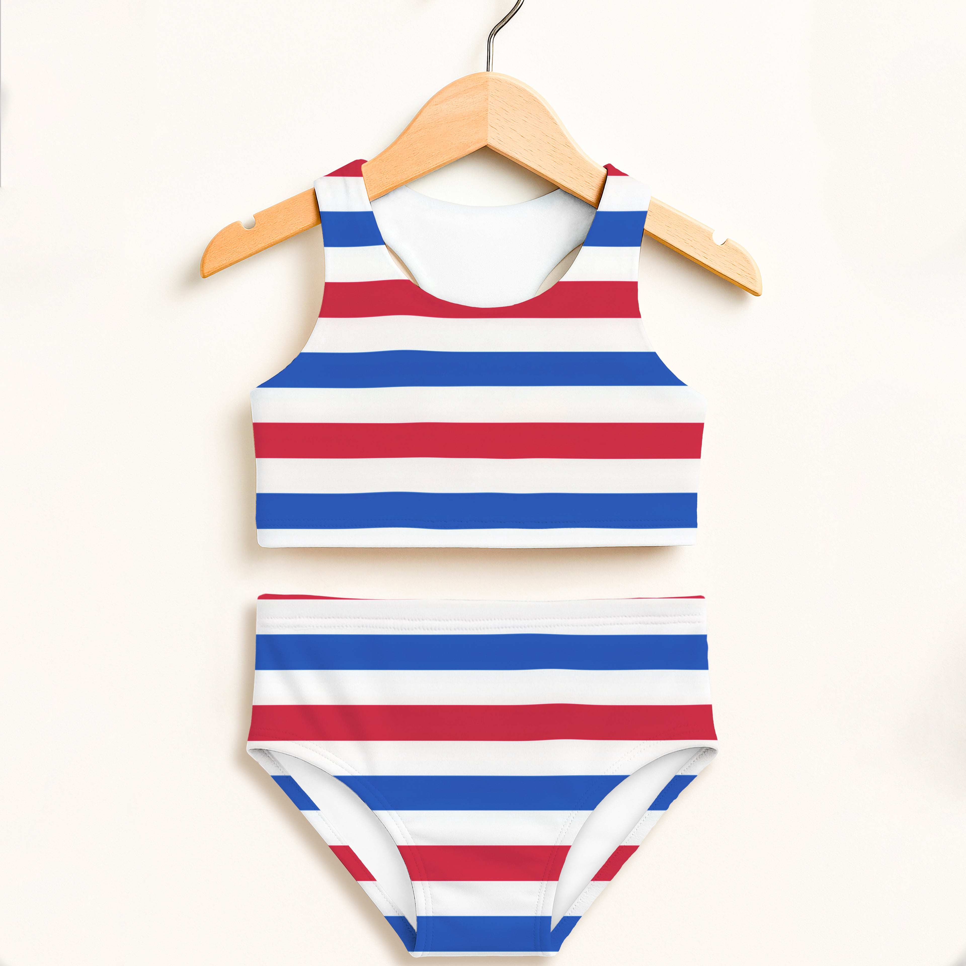 A vibrant red white and blue striped girls two piece swimsuit with double layered upf 50 plus fabric hanging on wooden hanger