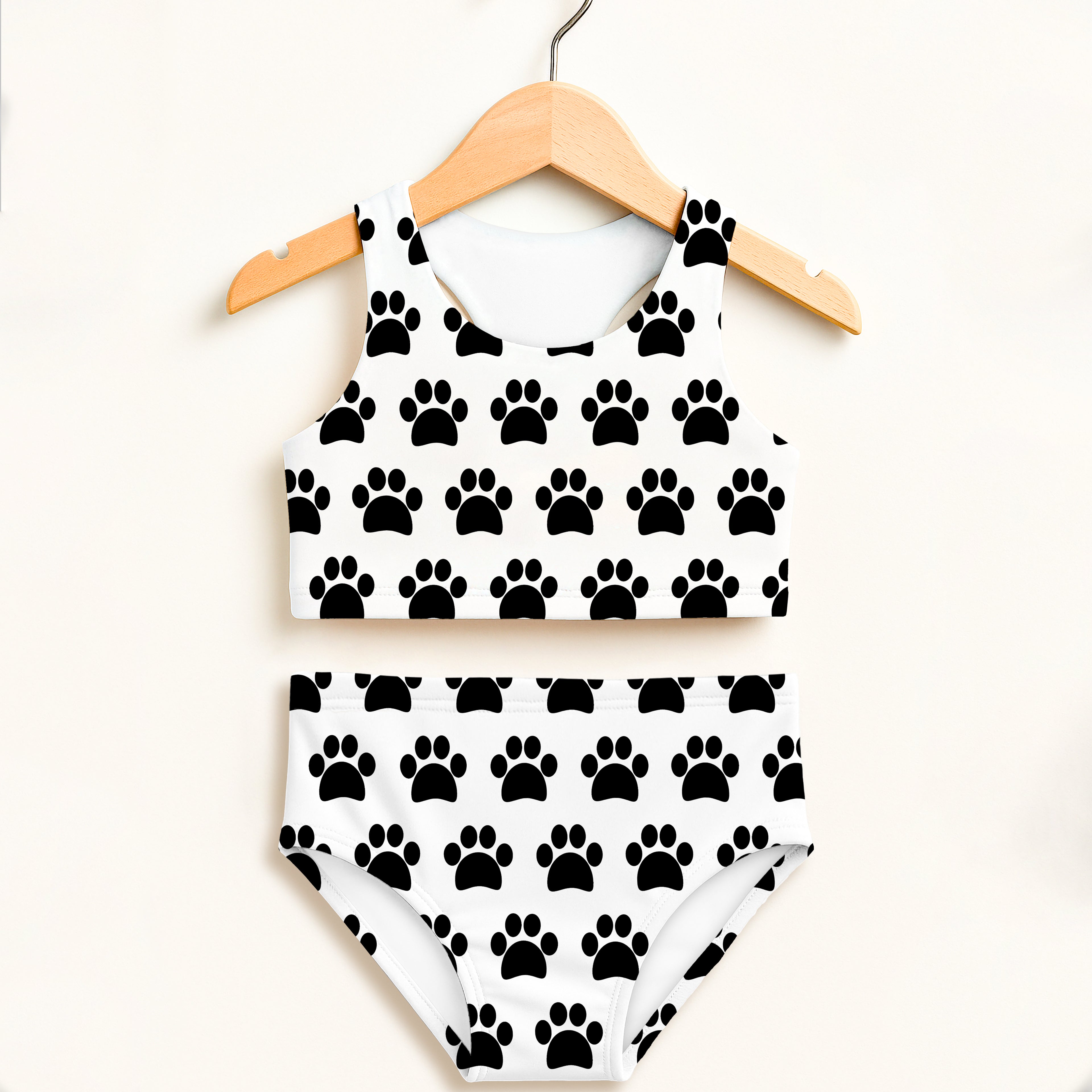 Girls white two piece swimsuit with black paw print pattern on wooden hanger featuring double layered upf 50+ fabric